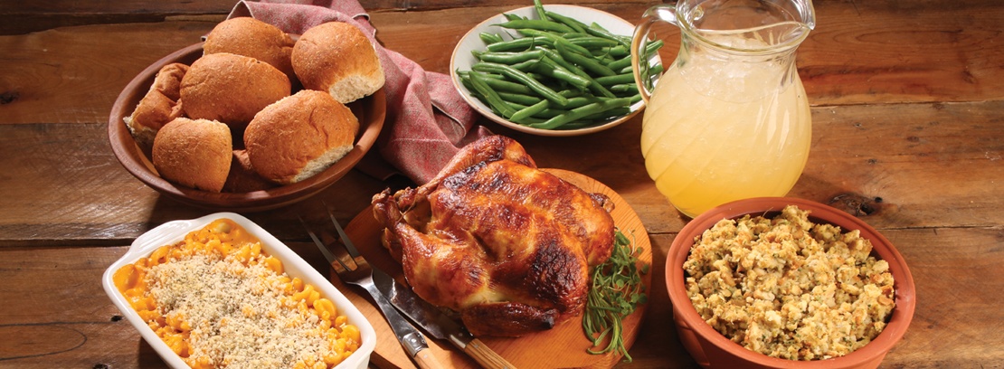 Roticerry chicken, green beans, corn, rolls and stuffing on wood table.